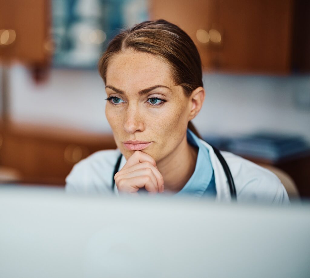 Pensive doctor working on her desktop PC at doctor's office.